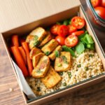 A vibrant meal prep box with pesto chicken, quinoa, and fresh veggies.